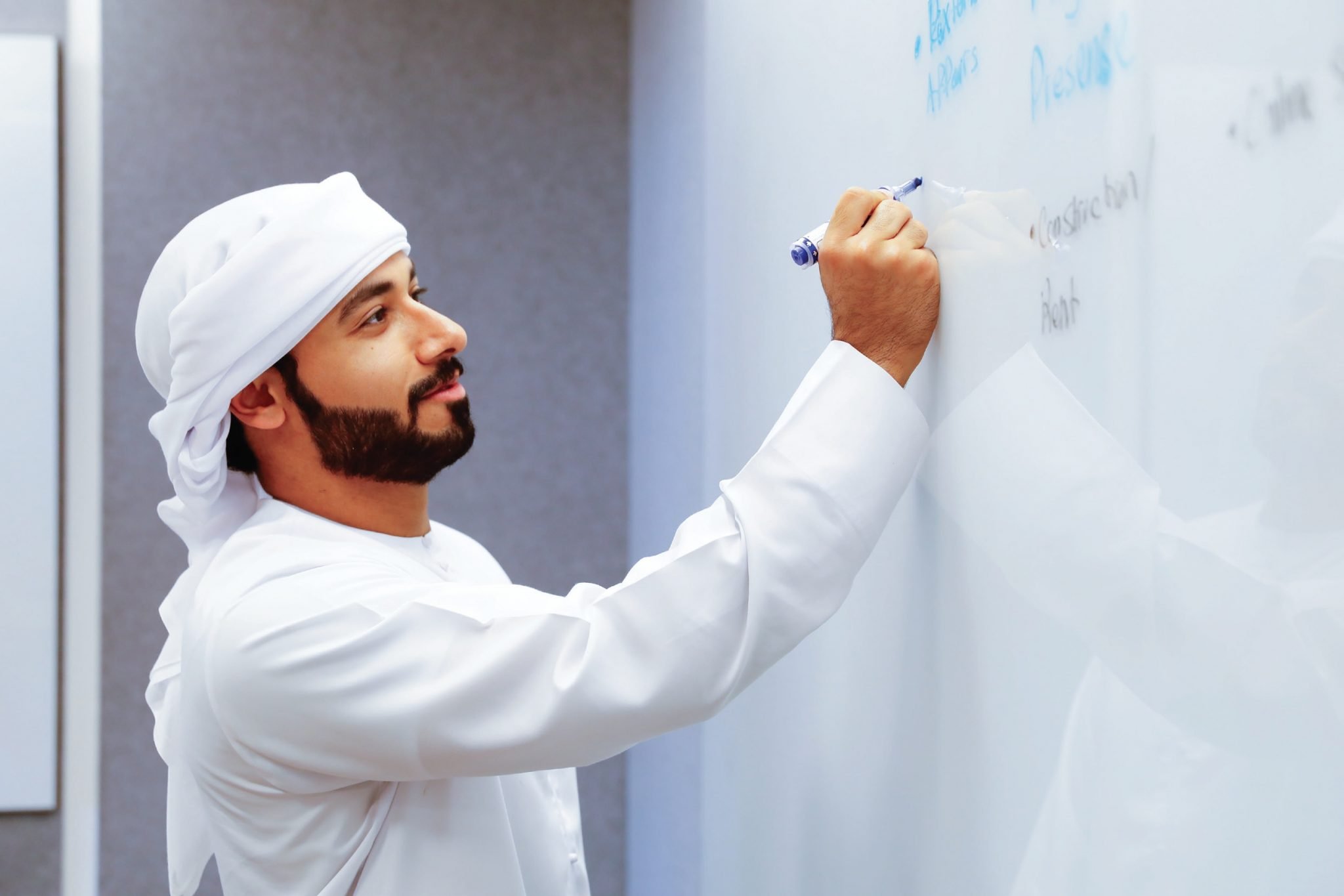 An Arab youth writing on a white board with a marker -  MIT Innovation Leadership Bootcamp by AGF, MIT and UAEU