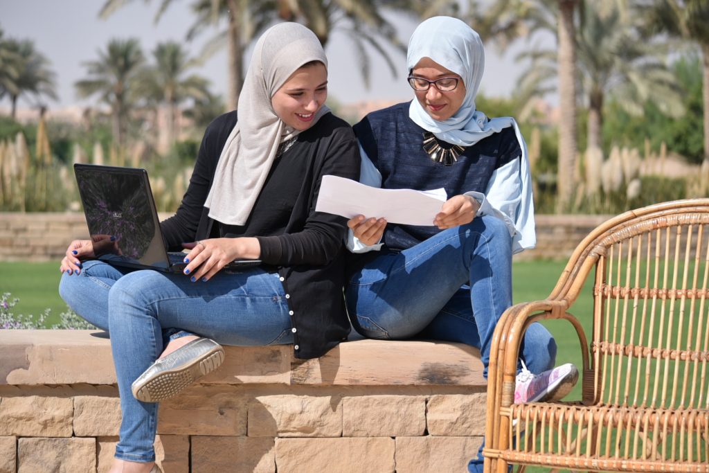 Two women students sitting outdoors and holding a laptop and document -Abdulla Al Ghurair Hub for Digital Teaching & Learning