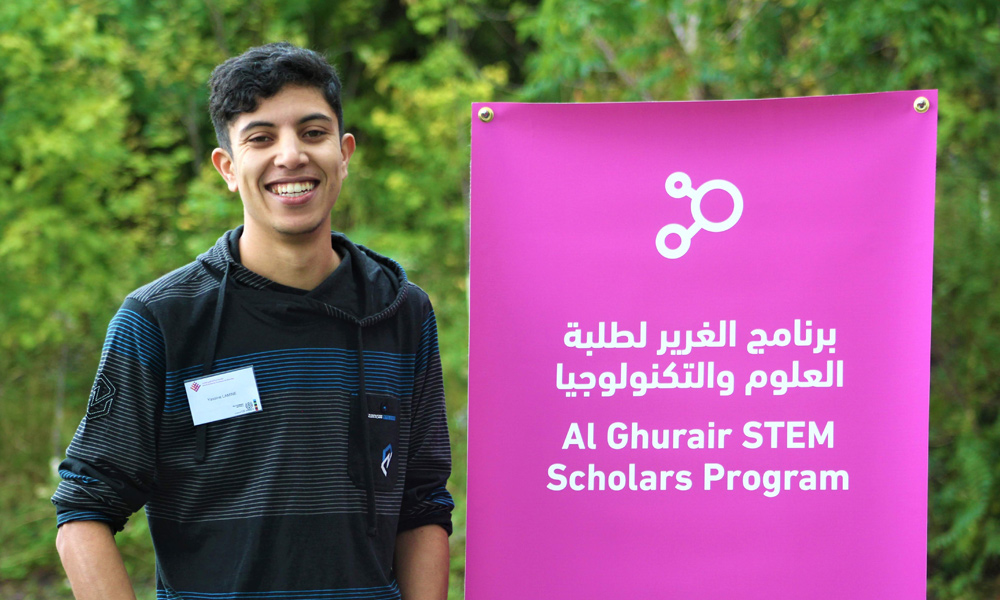 A young scholar stands in front of a sign for the Al Ghurair STEM Scholars Program that empowers Arab students in Education