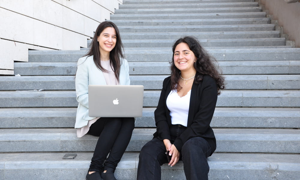 Two young scholars from AGF are seated on steps, utilizing a laptop to engage in AGF's digital learning platform.