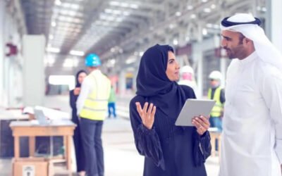 Two architects in traditional Emirati clothes standing on a construction site and talking. Woman is holding digital tablet. They look happy with results. There are some construction workers in back.