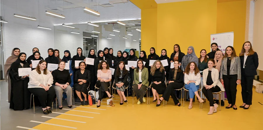 A group of women scholars poses for a photo indoors, holding certificates that indicate a graduation.