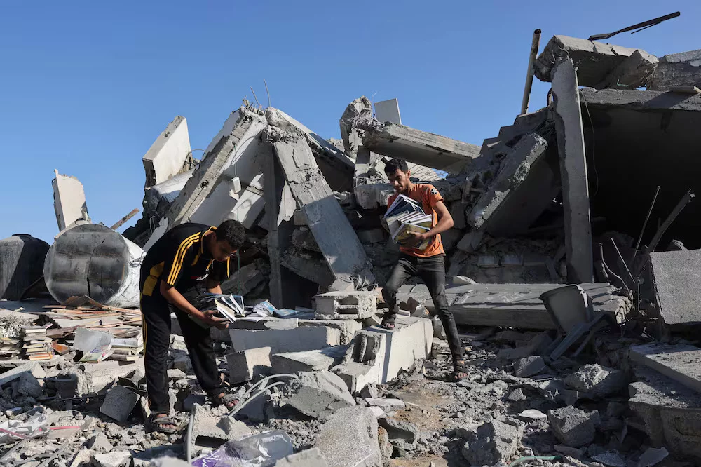 Two people in Gaza amid rubble, salvaging books from a collapsed concrete structure.