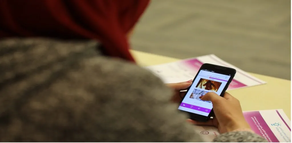 A student wearing a red head covering is using a smartphone, possibly for educational purposes-AGF