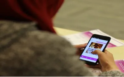 A student wearing a red head covering is using a smartphone, possibly for educational purposes-AGF