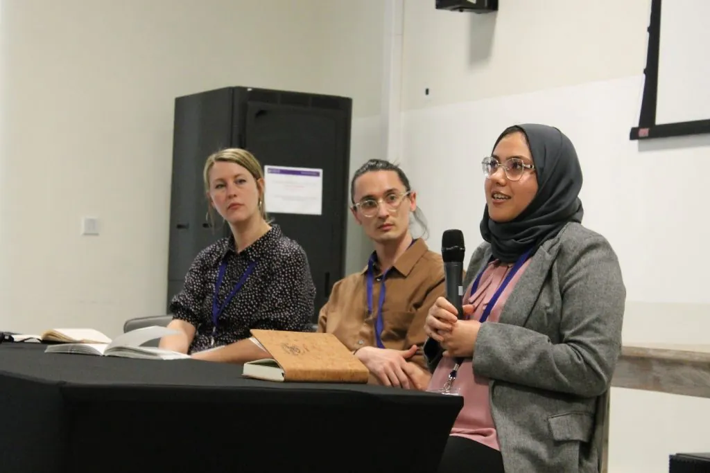 Three individuals participate in a panel discussion, indicating their role in a conference