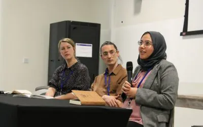 Three individuals participate in a panel discussion, indicating their role in a conference