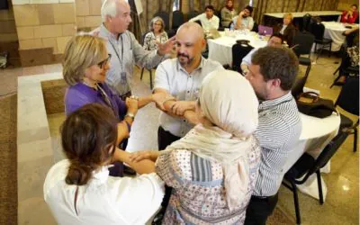 Six individuals stand in a circle, interlocking their arms and hands in a group activity