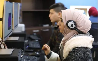 A group of individuals is attending an online training on desktop computers in a computer lab setting.