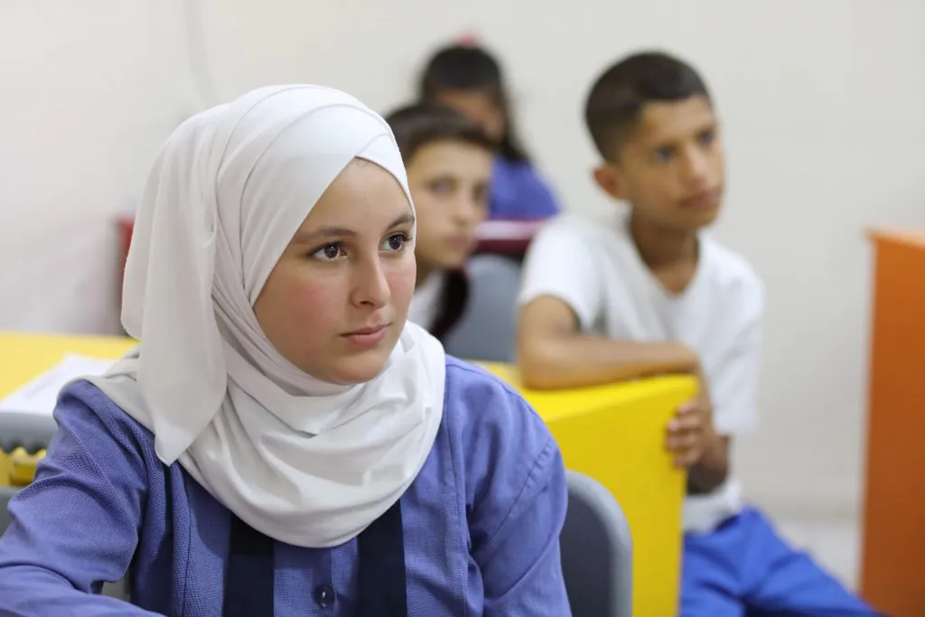 A classroom scene with several students seated at desks, appearing focused and attentive