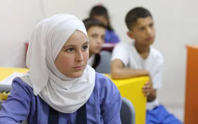 A classroom scene with several students seated at desks, appearing focused and attentive