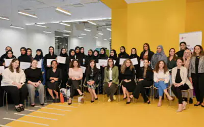 A group of women scholars poses for a photo indoors, holding certificates that indicate a graduation.